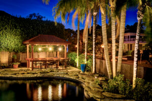 Layered lighting in luxury backyard with tiki hut and pool