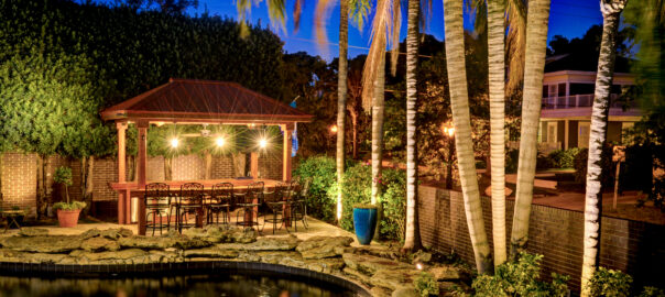 Layered lighting in luxury backyard with tiki hut and pool