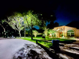 2 homes on a street, one well lit with landscape lighting and the other is dark